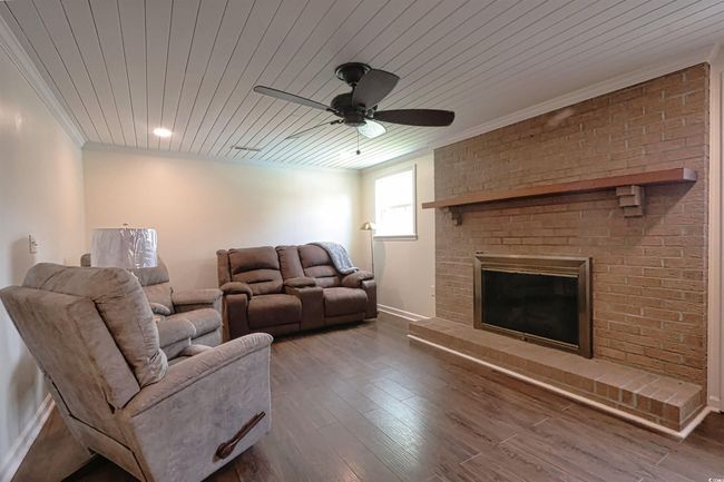 Living room with wooden ceiling, crown molding, ceiling fan, wood finished floors, and a brick fireplace | Image 7