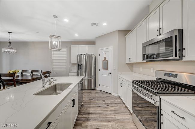 Kitchen featuring appliances with stainless steel finishes, a sink, light wood-type flooring, hanging light fixtures, and white cabinets | Image 22