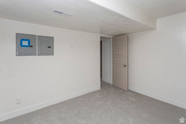 Basement with a textured ceiling, visible vents, electric panel, baseboards, and light carpet | Image 30