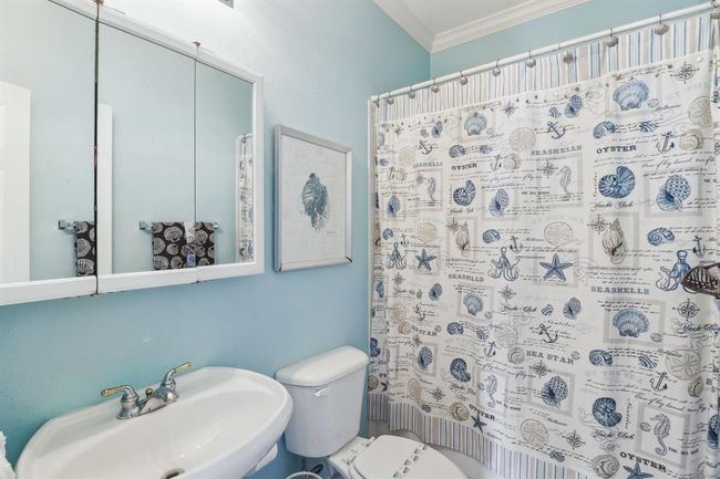 This charming secondary bathroom features a tub/shower combination, perfect for convenience and versatility. The coastal-inspired decor is highlighted by light blue walls and nautical accents, creating a refreshing and relaxing atmosphere. A mirrored medicine cabinet and pedestal sink provide functional storage and a clean, streamlined design. | Image 12