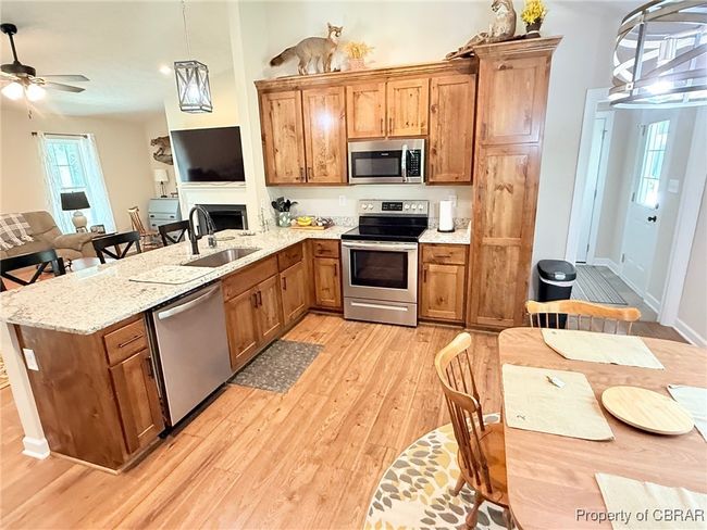 Kitchen featuring stainless steel appliances, a sink, waterproof Pergo flooring-wood-style floors, a peninsula, and Pine-stained cabinetry | Image 6