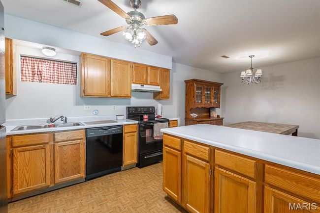 Kitchen featuring black appliances, under cabinet range hood, light countertops, a chandelier, and decorative light fixtures | Image 8