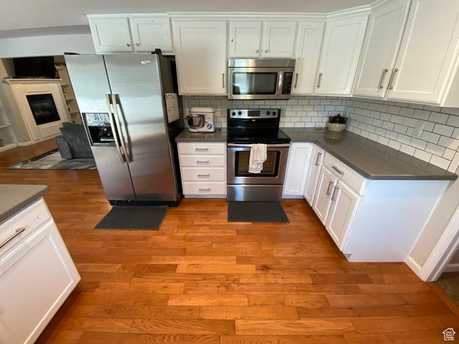 Kitchen with appliances with stainless steel finishes, light wood finished floors, dark countertops, and white cabinetry | Image 8