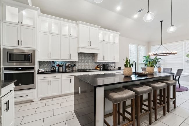 Kitchen with appliances with stainless steel finishes, dark countertops, light tile patterned flooring, decorative backsplash, and a chandelier | Image 12