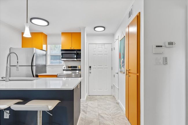 Kitchen featuring light marble finish flooring, stainless steel appliances, light countertops, decorative light fixtures, and a breakfast bar area | Image 4