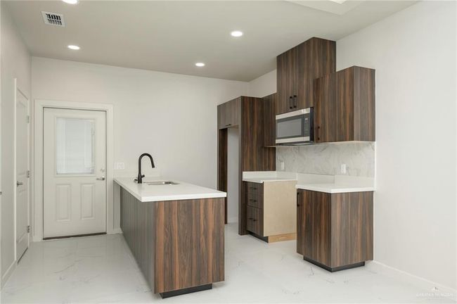 Kitchen with a sink, stainless steel microwave, light marble finish flooring, modern cabinets, and recessed lighting | Image 6