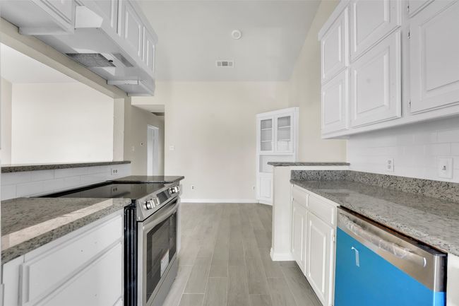 Kitchen with stainless steel range with electric cooktop, dishwasher, white cabinets, and light stone countertops | Image 7
