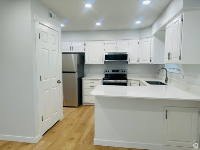 Kitchen with brand new stainless steel appliances, white cabinetry, light countertops, and light wood-style floors | Image 7
