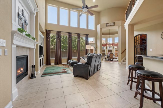 Living room with a towering ceiling, ceiling fan, stairs, a tiled fireplace, and light tile patterned floors | Image 9
