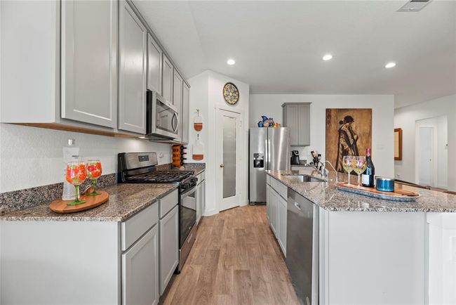The kitchen is equipped with sleek stainless steel appliances, adding a polished, modern touch. A corner pantry provides ample storage space, making it easy to keep everything organized. The sink is conveniently located on the island, offering both functionality and a central gathering spot for meal prep or casual conversation. With gray cabinets, granite countertops, and these thoughtful features, the kitchen is both stylish and highly functional, perfect for cooking and entertaining. | Image 7