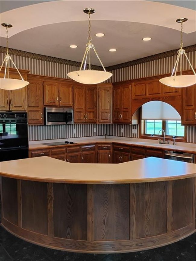 Kitchen with cooktop, light countertops, a sink, decorative light fixtures, and a kitchen island | Image 32