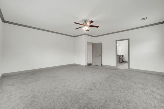 Unfurnished bedroom with ensuite bathroom, light colored carpet, ornamental molding, visible vents, and baseboards | Image 21
