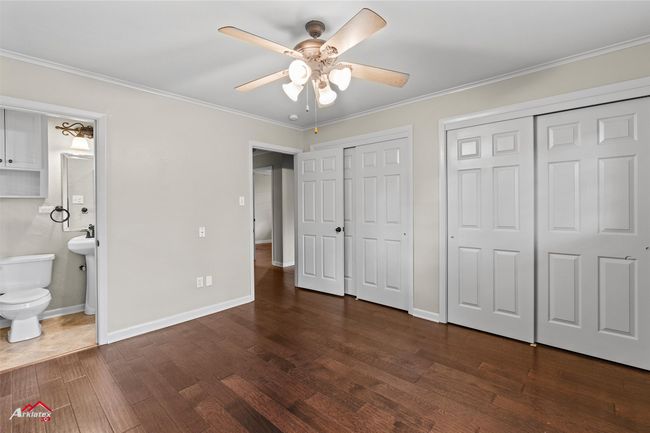 Unfurnished bedroom with two closets, dark wood-style floors, crown molding, baseboards, and ensuite bathroom | Image 16