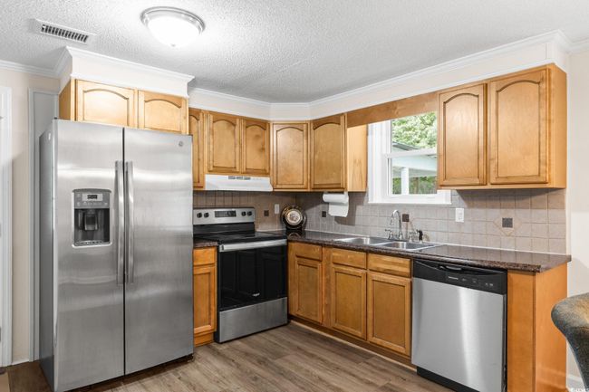 Kitchen featuring stainless steel appliances, under cabinet range hood, a sink, wood finished floors, and dark countertops | Image 22