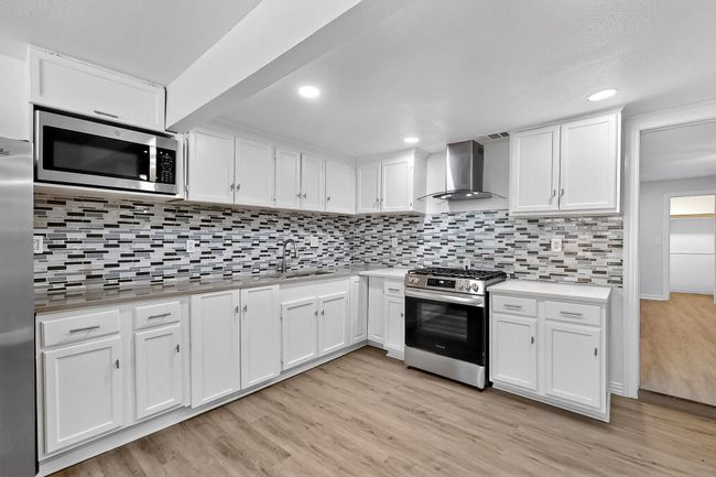 Kitchen featuring wall chimney exhaust hood, stainless steel appliances, light wood-style floors, white cabinetry, and backsplash | Image 26