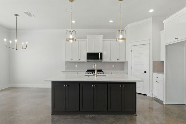 Kitchen featuring stainless steel microwave, finished concrete floors, decorative backsplash, white cabinetry, and recessed lighting | Image 6