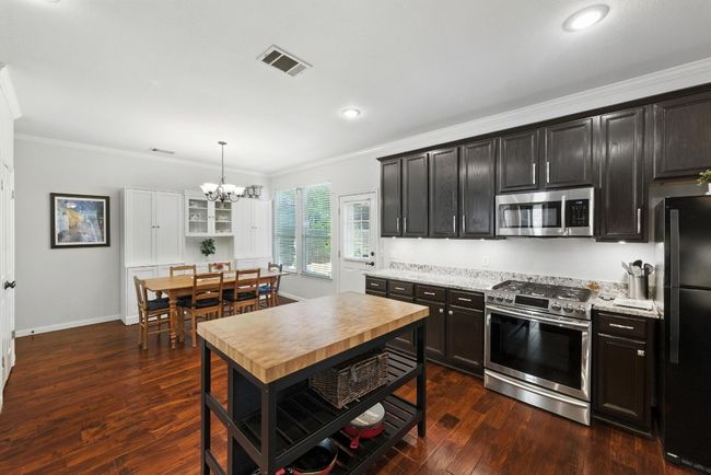 Kitchen featuring stainless steel appliances, crown molding, a chandelier, dark wood-style flooring, and pendant lighting | Image 8