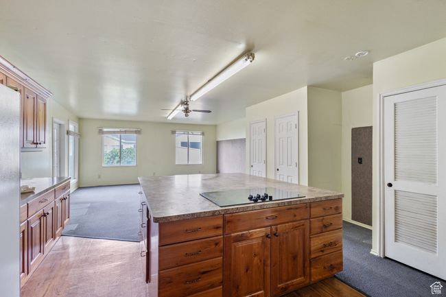 Kitchen featuring black electric cooktop, dark colored carpet, a ceiling fan, open floor plan, and a kitchen island | Image 8