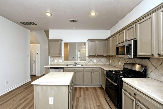 Kitchen with stainless steel appliances, light wood finished floors, a kitchen island, backsplash, and recessed lighting | Image 7