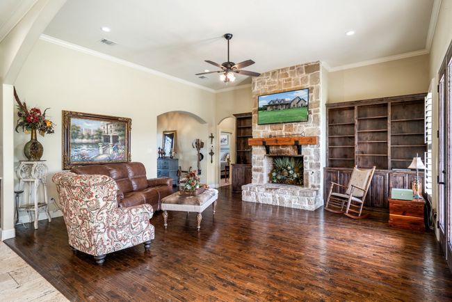 Living room with arched walkways, ceiling fan, hardwood / wood-style flooring, crown molding, and a stone fireplace | Image 12