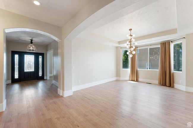 Entrance foyer leading to formal dining area with a chandelier, light wood-style floors, arched walkways, recessed lighting, and a raised ceiling | Image 6