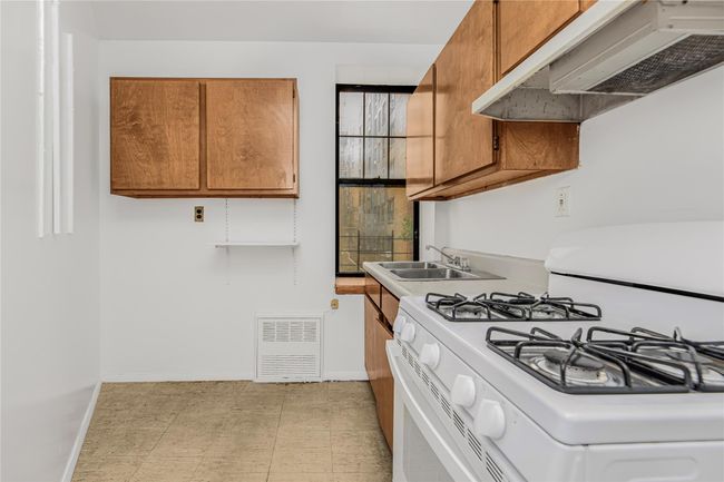 Kitchen with white range with gas stovetop, under cabinet range hood, brown cabinets, light countertops, and light flooring | Image 15