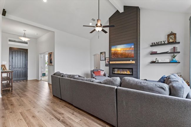 Living area with light wood finished floors, high vaulted ceiling, beamed ceiling, a ceiling fan, and a fireplace | Image 11