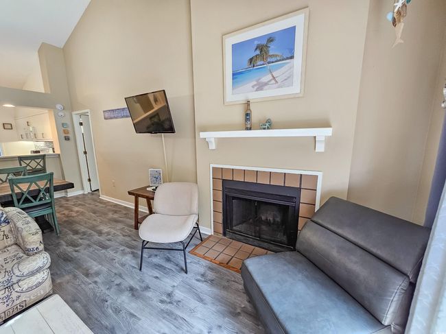 Living room featuring wood finished floors, a tiled fireplace, high vaulted ceiling, and baseboards | Image 8