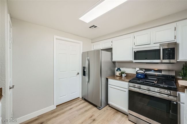 Kitchen featuring stainless steel appliances, baseboards, visible vents, light wood-style floors, and white cabinetry | Image 9