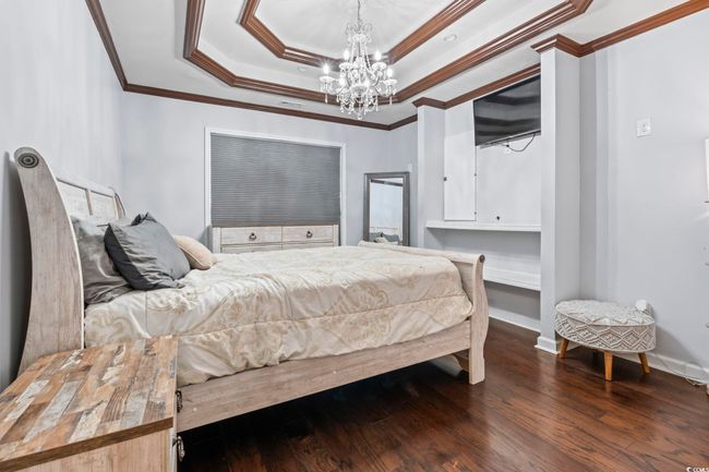Bedroom featuring a chandelier, crown molding, a tray ceiling, and wood finished floors | Image 19