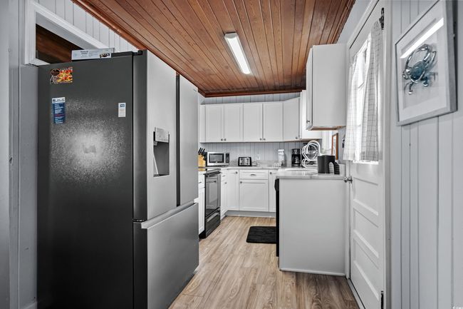 Kitchen featuring stainless steel appliances, a sink, wooden ceiling, light countertops, and white cabinets | Image 7