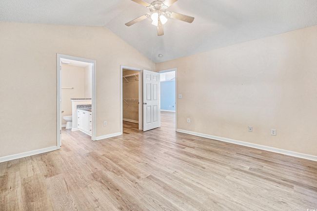 Unfurnished bedroom featuring a spacious closet, light wood finished floors, vaulted ceiling, ensuite bathroom, and ceiling fan | Image 21