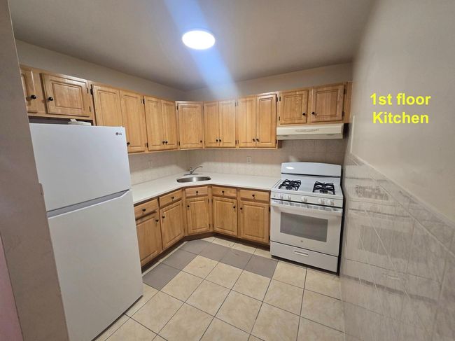 Kitchen featuring white appliances, under cabinet range hood, a sink, light tile patterned floors, and light countertops | Image 7