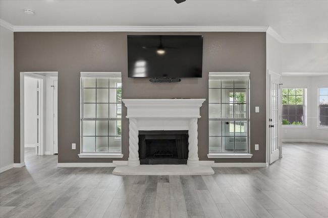 Unfurnished living room with baseboards, wood finished floors, a fireplace with raised hearth, and ornamental molding | Image 6