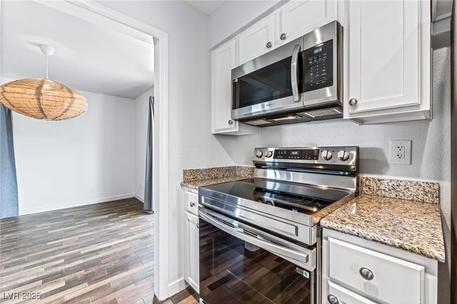 Kitchen featuring stainless steel appliances, wood finished floors, white cabinets, and light stone countertops | Image 16