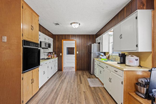 Kitchen featuring stainless steel appliances, light countertops, light wood-type flooring, a textured ceiling, and wooden walls | Image 18