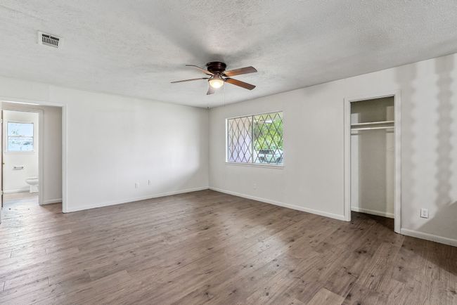Unfurnished bedroom with a textured ceiling, multiple windows, wood finished floors, a closet, and ceiling fan | Image 6