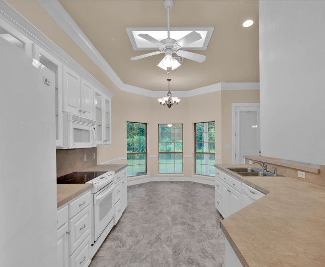 Kitchen with white appliances, a skylight, white cabinets, ceiling fan, and crown molding | Image 14