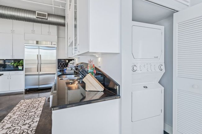 Kitchen featuring stacked washer / dryer, stainless steel built in fridge, white cabinetry, Ink granite countertops, and glass insert cabinets | Image 9