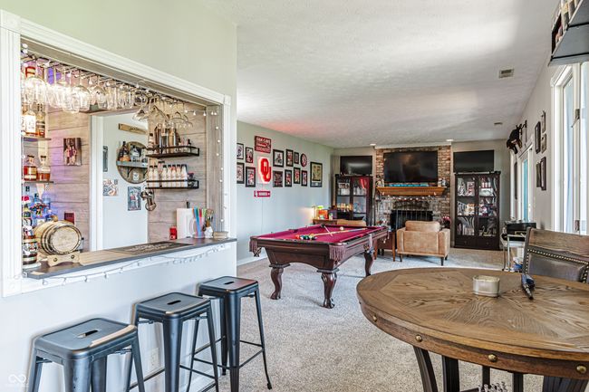 game room featuring a textured ceiling, carpet, a bar, and a brick fireplace | Image 36