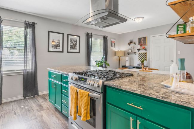 Kitchen featuring stainless steel gas range, island range hood, light wood finished floors, baseboards, and light stone counters | Image 14