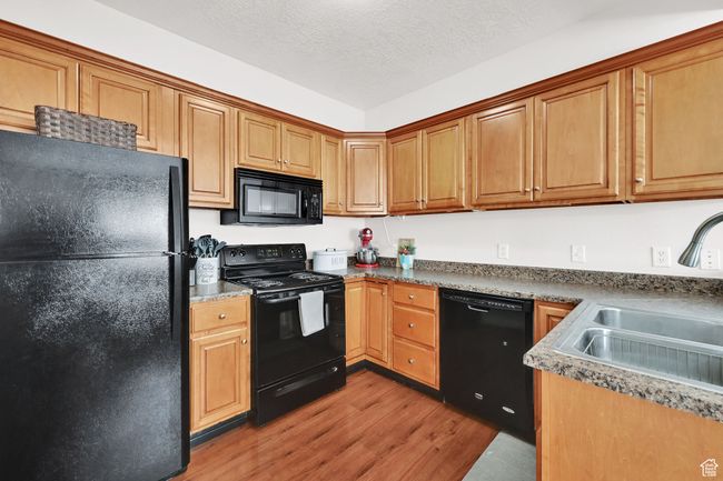 Kitchen featuring brown cabinets, black appliances, a sink, a textured ceiling, and light wood finished floors | Image 22