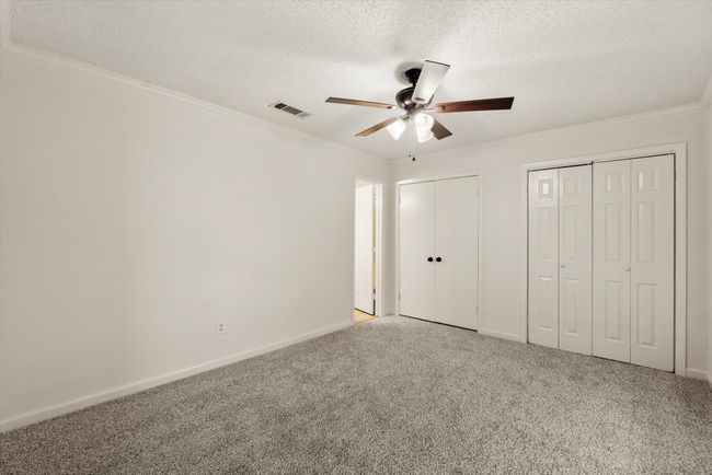 Unfurnished bedroom with crown molding, ceiling fan, carpet, a textured ceiling, and multiple closets | Image 21