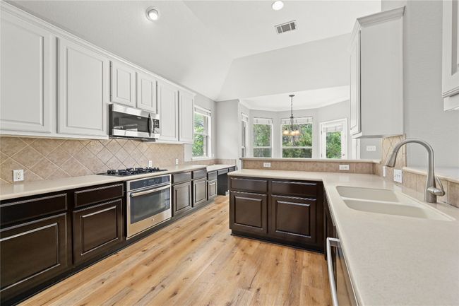Kitchen featuring light wood-style flooring, appliances with stainless steel finishes, white cabinets, a sink, and visible vents | Image 12