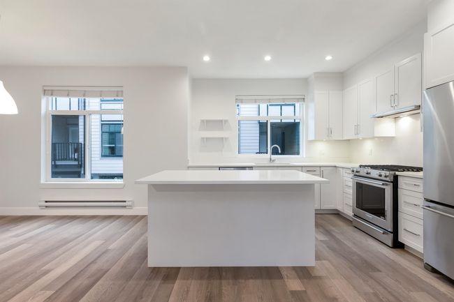 Kitchen featuring a baseboard radiator, a sink, light countertops, appliances with stainless steel finishes, and a kitchen island | Image 7