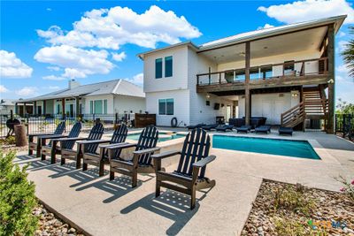 he back of the home offers a stunning water view of the bay with a spacious outdoor entertainment area, a swimming pool and enough space for lounging. The upper level boasts a covered balcony, and there's a well-maintained lawn enclosed by a fence. | Image 3