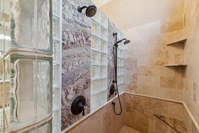 The walk-in shower in the primary suite is encompassed in travertine tile with a porcelain tiled floor and illuminated by a crystal chandelier. Dual shower heads saturate while a heat lamp protects from any chilly draft! | Image 21