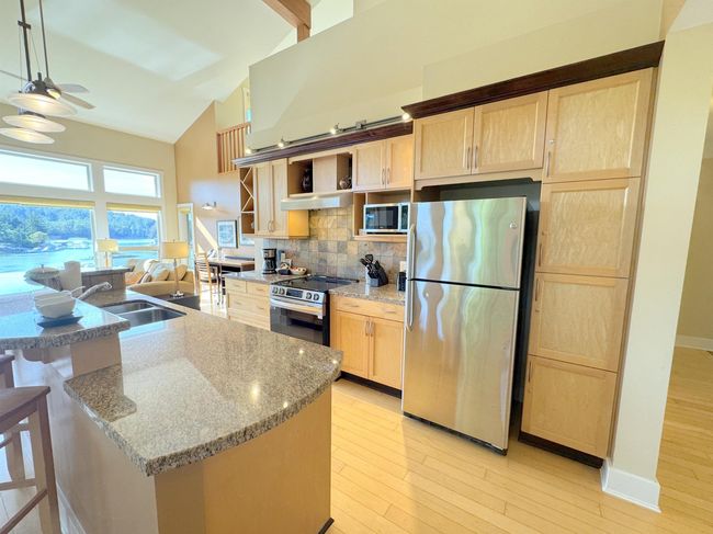 Kitchen with stainless steel appliances, high vaulted ceiling, light brown cabinets, open shelves, and tasteful backsplash | Image 5