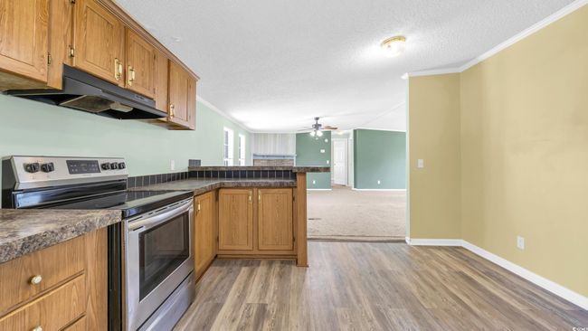 Kitchen with stainless steel electric range oven, under cabinet range hood, ceiling fan, crown molding, and a textured ceiling | Image 8
