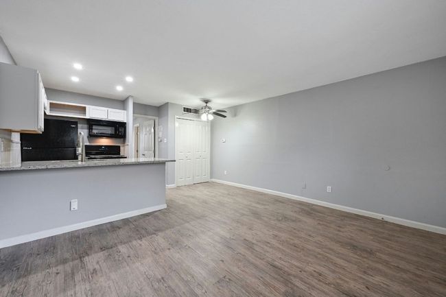 Kitchen featuring white cabinets, light stone countertops, light wood finished floors, ceiling fan, and black appliances | Image 8